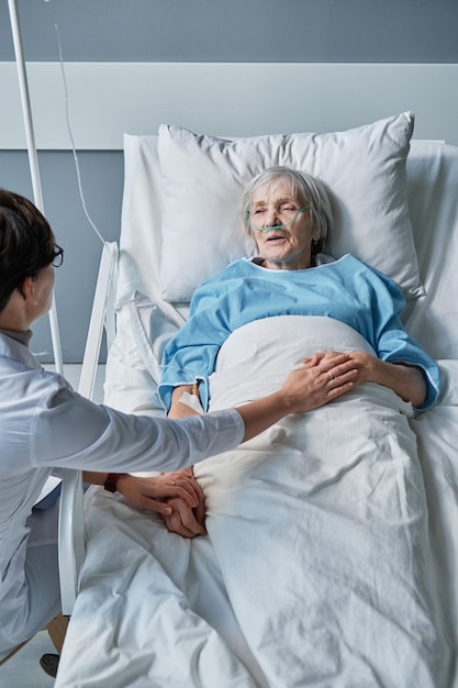 Vue grand angle du médecin tenant la main d'une femme âgée et la soutenant pendant la maladie à l'hôpital