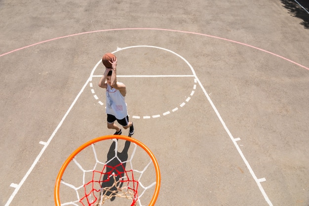 Vue grand angle du panneau arrière du jeune homme athlétique prenant une photo sur un terrain de basket-ball en plein air