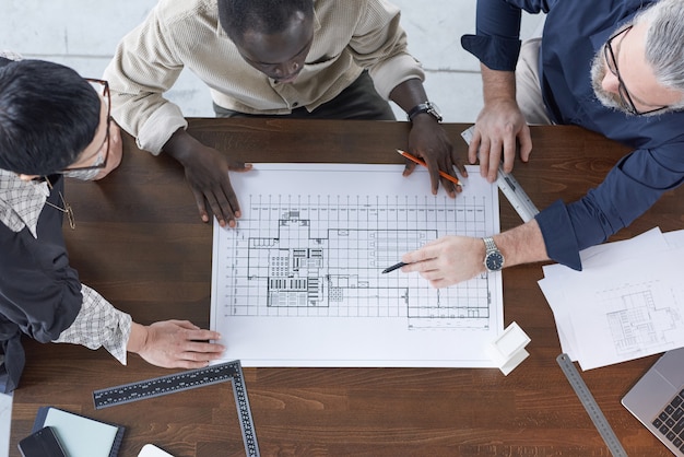 Vue grand angle du plan sur la table avec des ingénieurs l'examinant et discutant en équipe au bureau