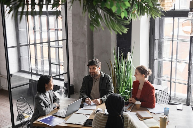 Vue en grand angle sur une équipe commerciale diversifiée discutant du projet à la table de réunion se concentre sur un homme barbu souriant à ses collègues, espace de copie