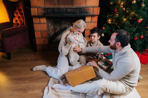 Vue grand angle d'une famille heureuse avec un joli chat assis avec des cadeaux de vacances par l'arbre de noël et