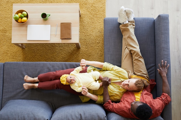 Vue grand angle de la famille de trois reposant sur un canapé avec leur petite fille