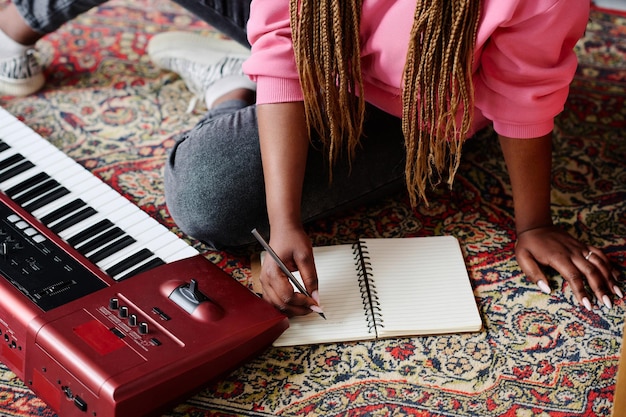 Vue grand angle d'une femme afro-américaine assise sur le sol et écrivant une chanson dans son cahier