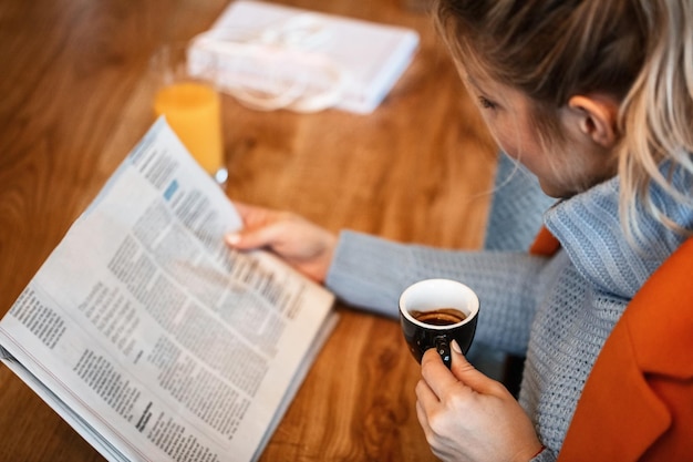 Vue grand angle de la femme buvant du café et lisant le journal quotidien tout en se relaxant dans un café L'accent est mis sur la tasse de café