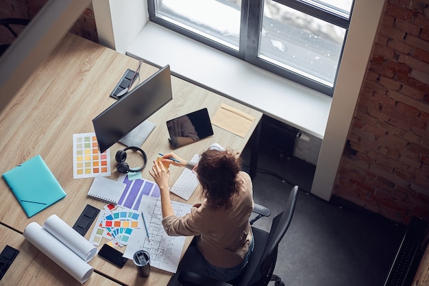 Vue grand angle d'une femme designer utilisant des notes autocollantes travaillant sur un nouveau projet de design d'intérieur