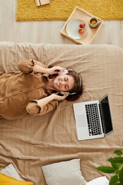 Vue grand angle d'une fille heureuse aux yeux fermés allongée sur le lit et écoutant de la musique au casque