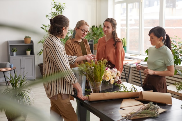 Vue grand angle sur un groupe diversifié de jeunes fleuristes organisant des compositions florales tout en travaillant dans un magasin de fleurs