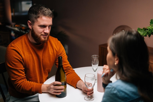 Vue grand angle d'un jeune homme versant du vin dans un verre pendant qu'il parlait avec sa femme assise ensemble à une table de fête