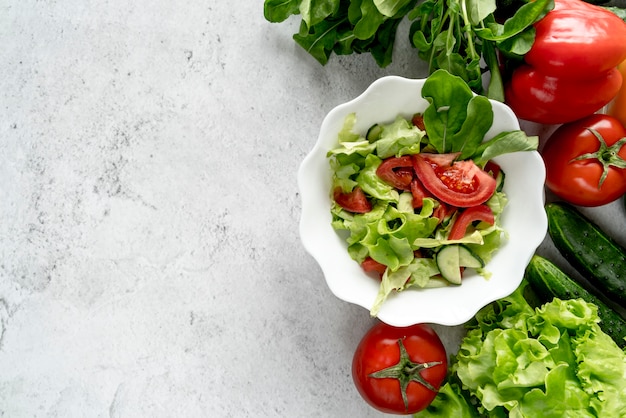 Photo vue grand angle de légumes entiers avec bol de salade sur fond texturé