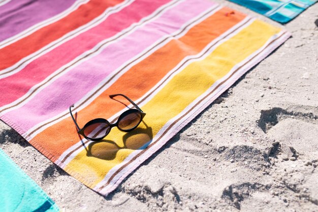 Vue grand angle des lunettes de soleil et des serviettes colorées sur la plage de sable pendant la journée ensoleillée. Espace de copie, inchangé, protection, vacances, mode, pique-nique et concept d'été.