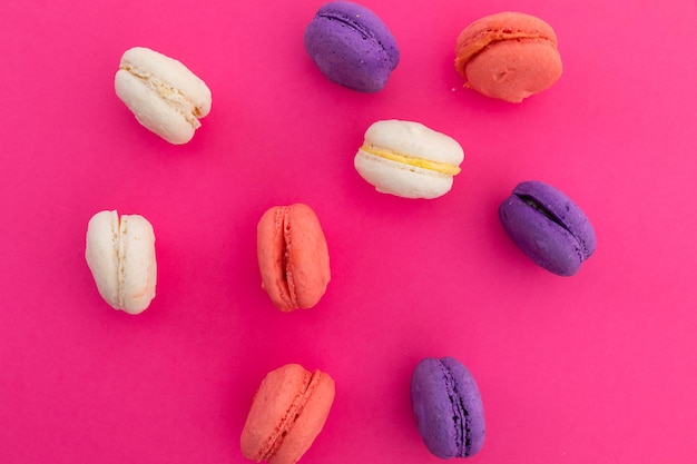 Vue grand angle de macarons violets, roses et blancs sur fond rose. concept de nourriture amusante de dessert frais.