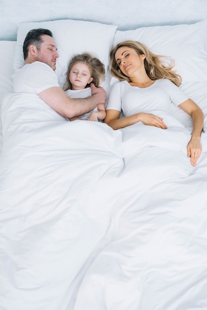 Vue grand angle de la mère; fille et père reposant sur un lit blanc