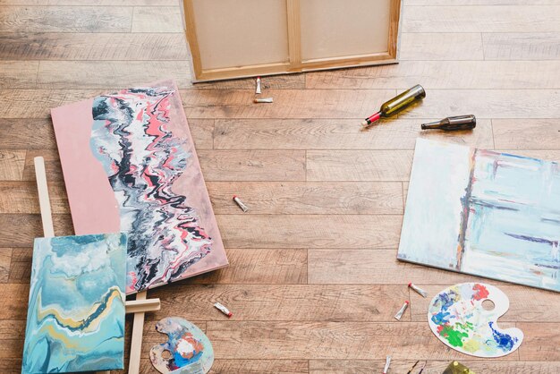 Vue grand angle de peintures dessiner des ustensiles et des bouteilles vides sur un plancher en bois dans un studio de peinture