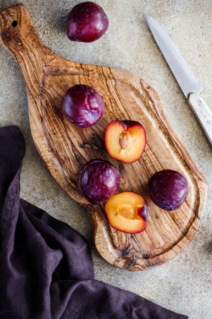 Vue grand angle de prune violette fraîche sur une planche à découper en bois texturée