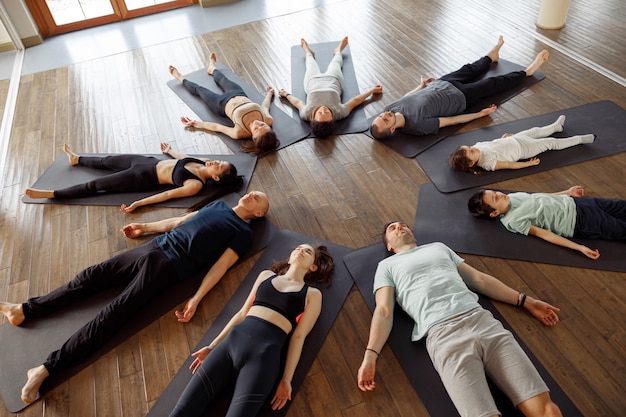 Vue d'un grand groupe de jeunes allongés sur un tapis de yoga en cercle, s'étirant dans un cours de yoga.