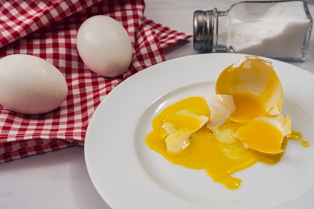 Vue grignotée d'un œuf de poule cassé sur une assiette blanche à côté de deux œufs sains sur une serviette de table.