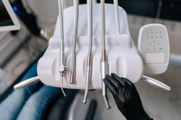 Vue en gros plan du haut d'un dentiste irréconnaissable dans des gants en caoutchouc prenant une perceuse dentaire électrique d'un ensemble d'outils dentaires pour traiter un patient souffrant de maux de dents dans une clinique dentaire Concept de blanchiment des dents