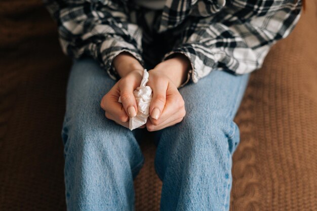 Vue en gros plan d'une femme en pleurs méconnaissable tenant des mouchoirs en papier dans les mains et les fouillant nerveusement à la maison