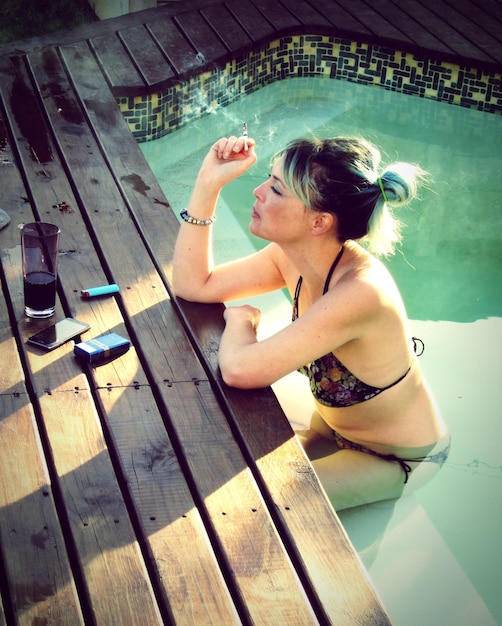 Vue à haut angle d'une femme fumant une cigarette assise dans une piscine