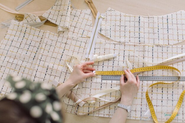 Vue à haut angle d'une femme mesurant un tissu avec une bande et une règle sur la table