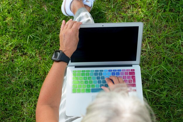Photo vue à haut angle d'une femme utilisant un ordinateur portable alors qu'elle est assise sur un champ herbeux