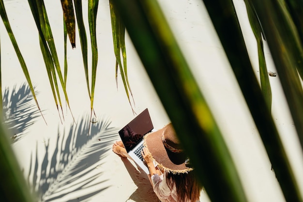 Vue à haut angle d'une femme utilisant un ordinateur portable alors qu'elle est assise sur la plage vue à travers les feuilles