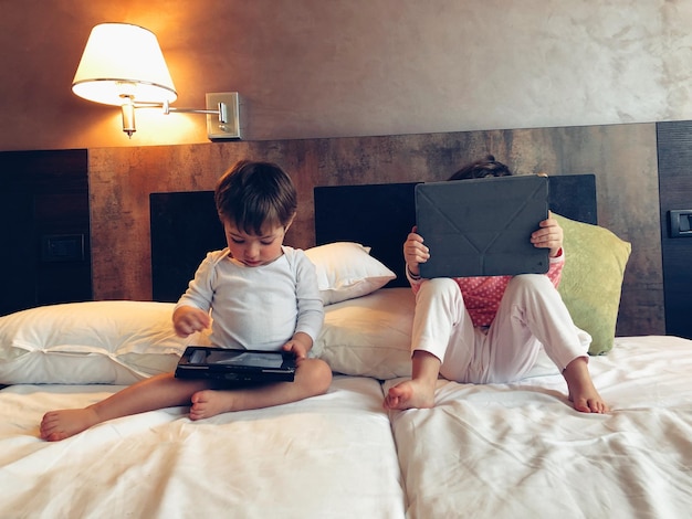 Vue à haut angle des frères et sœurs avec la technologie assis sur le lit à la maison.