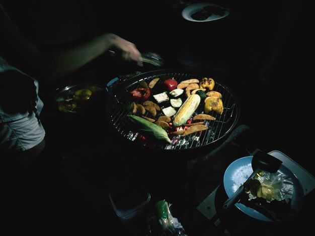 Photo vue à haut angle d'une personne cuisinant de la nourriture sur un gril au barbecue la nuit