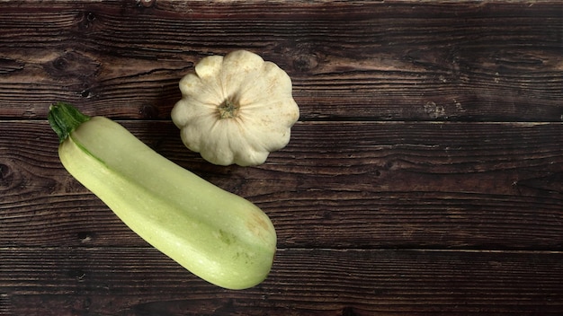 Vue de haut en bas, courge pâtisson et courgette sur une planche en bois sombre, large bannière, espace pour le texte à droite