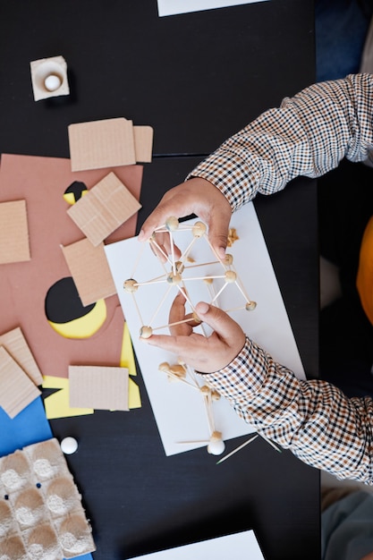 Vue de haut en bas sur un enfant méconnaissable fabriquant des modèles en carton pendant un cours d'art et d'artisanat à l'école avec une enseignante, espace de copie