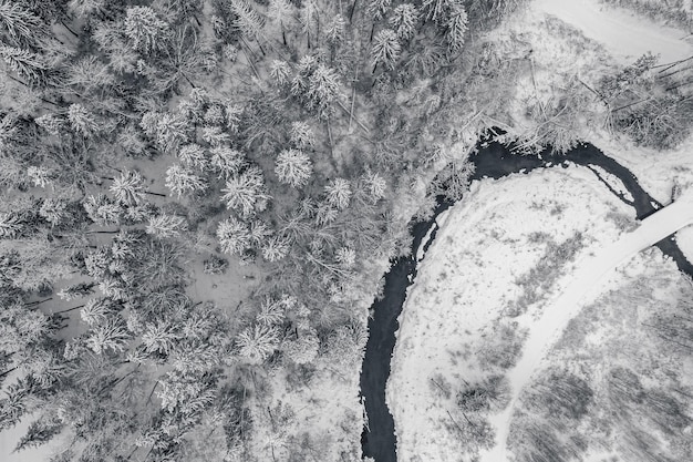 Vue de haut en bas d'une forêt de sapins d'hiver, d'une rivière étroite et d'une route entièrement recouverte de neige