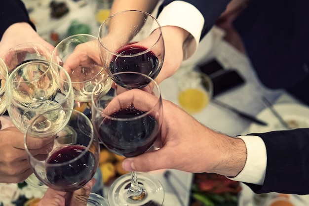 Vue de haut en bas des mains masculines et féminines avec des verres de vin remplis au-dessus de la table du restaurant. Boire des toasts et des gobelets tintants lors d'un dîner. Boire du vin lors d'un banquet. Fêtez un événement.