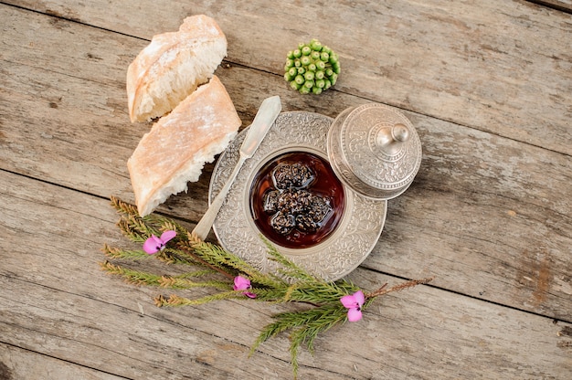 Photo vue d'en haut sur la confiture de cônes dans la plaque d'argent avec une casquette, une branche d'arbre et du pain à proximité sur la table en bois