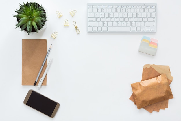 Vue d'en haut du lieu de travail avec clavier d'ordinateur, ordinateur portable, fleur en pot verte, enveloppes artisanales et téléphone portable, poser à plat.