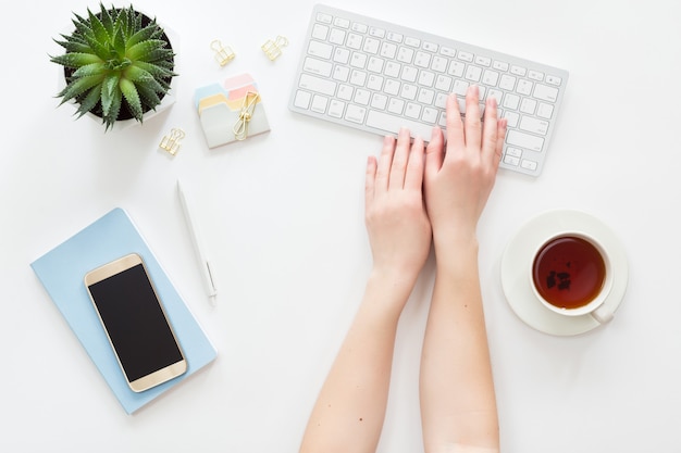 Vue d'en haut du milieu de travail femme avec clavier d'ordinateur, ordinateur portable, fleur en pot verte et téléphone portable, poser à plat.