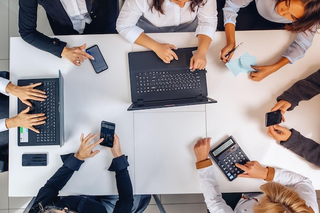 Vue d'en-haut. Une équipe commerciale concentrée et confiante travaillant ensemble assise à une table dans un bureau moderne utilisant un ordinateur portable et des téléphones. Concept de charge d'équipe.
