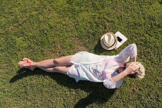 Photo vue d'en haut d'une femme allongée et se détendant sur un pré couvert d'herbe verte un jour ensoleillé d'été ou de printemps. concept de loisirs, d'éducation, d'étude, de curiosité, de loisirs en famille.