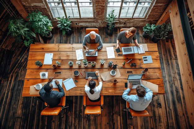 Vue d'en haut d'un groupe diversifié de cinq professionnels travaillant ensemble à une grande table en bois dans un bureau moderne