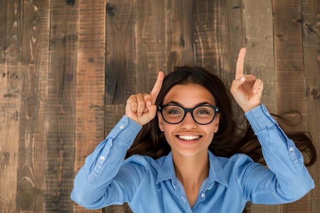 Photo vue d'en haut d'une jeune femme souriante assise à une table et pointant vers le haut dans le bureau