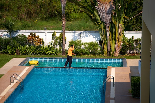 Vue d'en haut d'un ouvrier nettoyant une piscine dans une maison privée en été