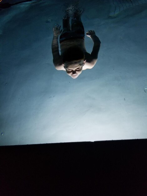 Photo vue haute angle d'un garçon sans chemise nageant dans une piscine éclairée la nuit