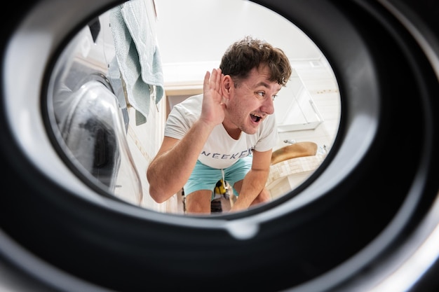 Vue de l'homme depuis la machine à laver à l'intérieur L'homme fait la routine quotidienne de la lessive Écoute le son à l'intérieur