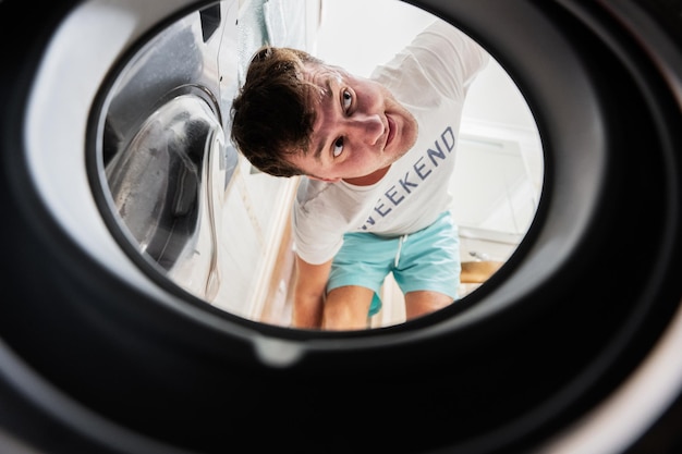 Vue de l'homme depuis la machine à laver à l'intérieur de Male fait la routine quotidienne de la lessive