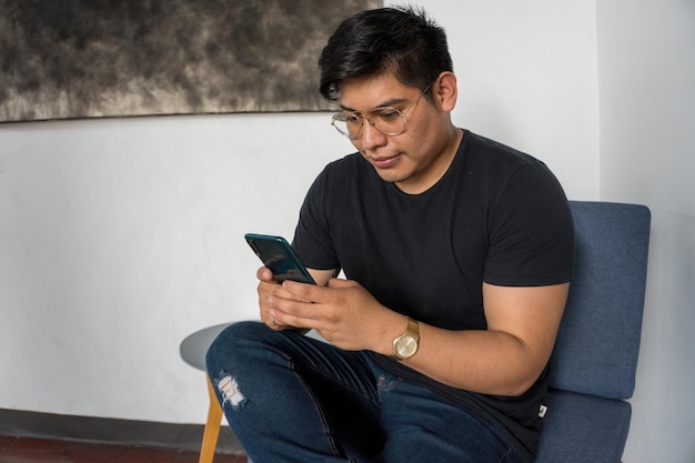 Vue d'un homme hispanique portant des lunettes et un t-shirt noir faisant quelque chose sur son téléphone