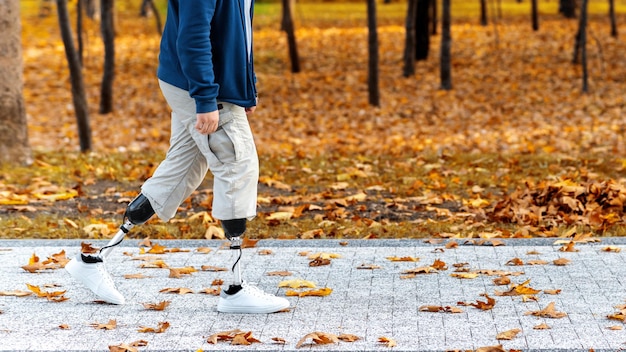 Vue d'un homme marchant avec des jambes prothétiques et des baskets blanches Feuilles jaunes tombées sur le sol