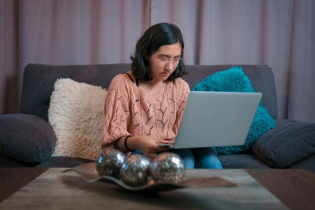 Vue horizontale d'un adolescent assis sur le canapé avec son ordinateur portable, elle fait attention à l'appel vidéo prend une classe virtuelle