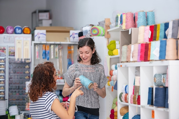 Vue horizontale de l'aide assistant sur un magasin de détail aidant une femme à acheter une pelote de laine bleue