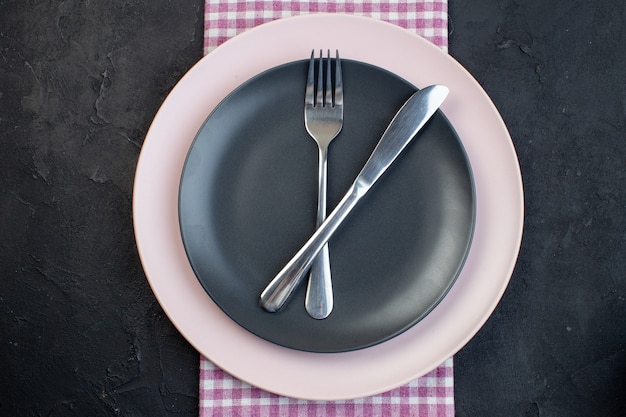 Photo vue horizontale de couverts en acier inoxydable sur des assiettes vides en céramique colorées sur une serviette rose sur fond noir avec espace libre