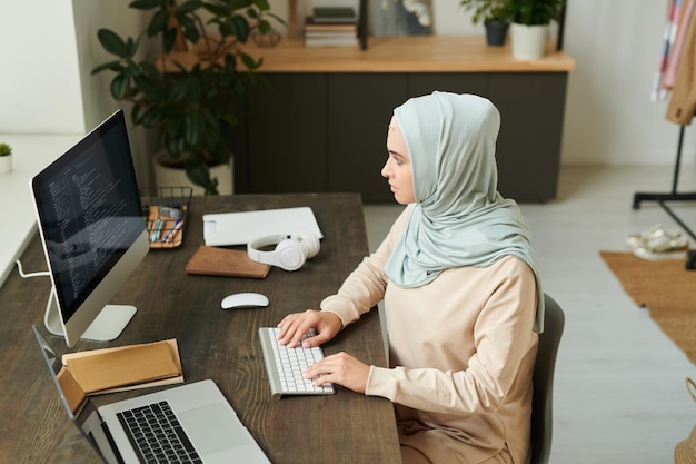 Vue horizontale en grand angle d'une jeune femme musulmane moderne travaillant sur la programmation à l'aide de bureau co