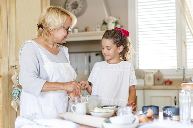 Vue horizontale. Grand-mère et adorable petite-fille frisée en cuisine, elles se préparent ensemble.